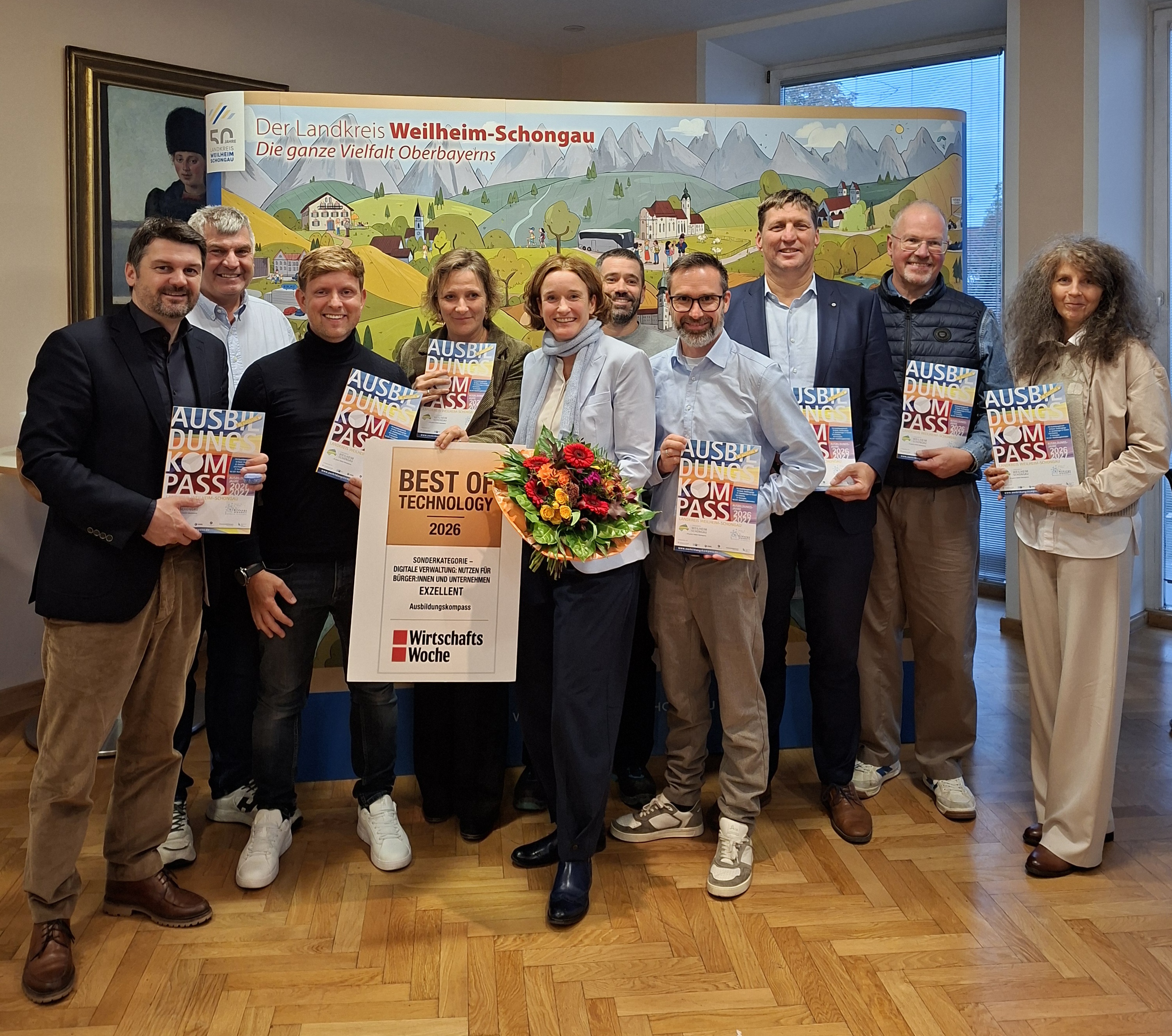 Gruppenfoto zur Auszeichnung des Ausbildungskompasses Weilheim-Schongau mit dem Best of Technology Award 2026. Die Beteiligten halten Ausbildungskompasse, in der Mitte stehen Monika Uhl mit Blumenstrauß und die Auszeichnung.