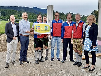 LEADER-Förderung für Bergwacht Benediktbeuern Vertreter der LEADER-Aktionsgruppe Bad Tölz-Wolfratshausen und der Bergwacht Benediktbeuern stehen vor der Baustelle der geplanten Ausbildungs- und Fahrzeughalle.