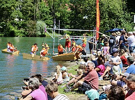 Zuschauerinnen und Zuschauer verfolgen die Sautrogregatta am Loisachufer in Wolfratshausen.