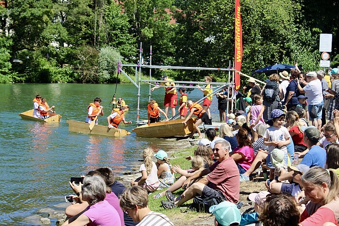 Zuschauerinnen und Zuschauer verfolgen die Sautrogregatta am Loisachufer in Wolfratshausen.