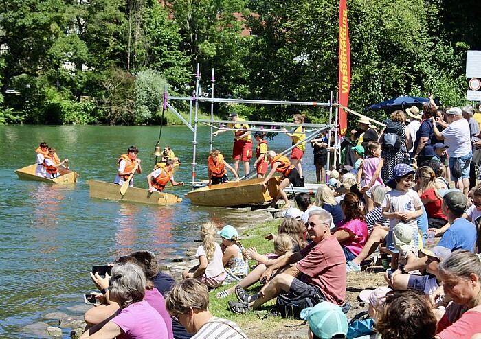 Zuschauerinnen und Zuschauer verfolgen die Sautrogregatta am Loisachufer in Wolfratshausen.