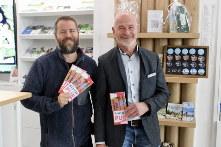 Kultur pur 2027 – Programmvorstellung in Wolfratshausen Kulturmanager Andreas Kutter und Bürgermeister Klaus Heilinglechner stehen mit den Programmflyern „Kultur pur 2027“ in der Tourist-Information Wolfratshausen.