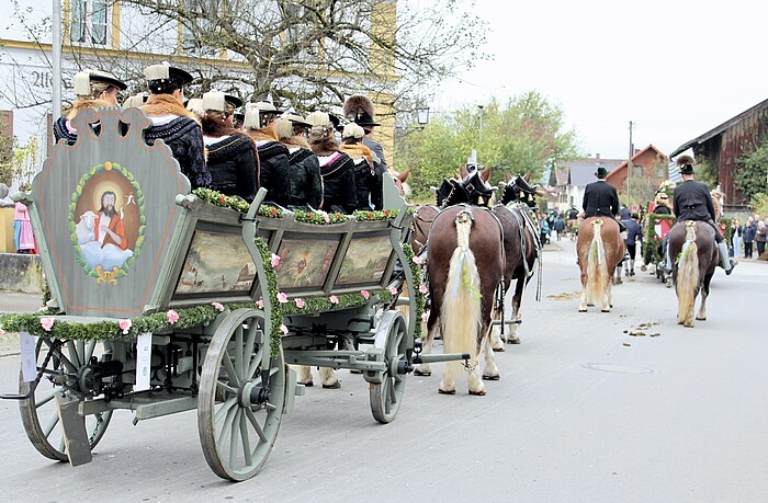 Von Pferden gezogener, mit Blumen geschmückter Festwagen mit Frauen in traditionellen Trachten bei der Leonhardifahrt in Benediktbeuern.