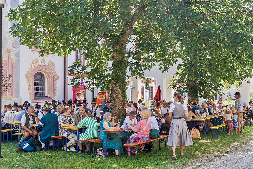 Jahrmarkt im Kloster Beuerberg Besucherinnen und Besucher sitzen beim Jahrmarkt im Kloster Beuerberg an Bierbänken unter Bäumen.