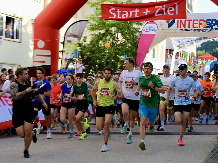 Läufer starten beim Alpenland Firmenlauf 2026 in Geretsried unter dem Startbogen