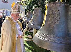 Kardinal Reinhard Marx steht mit einem Schlägel vor einer der vier neuen Bronzeglocken der Stiftskirche St. Peter und Paul in Beuerberg.