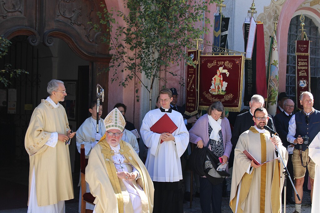 Glockenweihe in Beuerberg – Geistliche und Festgäste Kardinal Reinhard Marx sitzt vor der Stiftskirche, umgeben von Geistlichen, Ministranten und weiteren Teilnehmern der Feier.